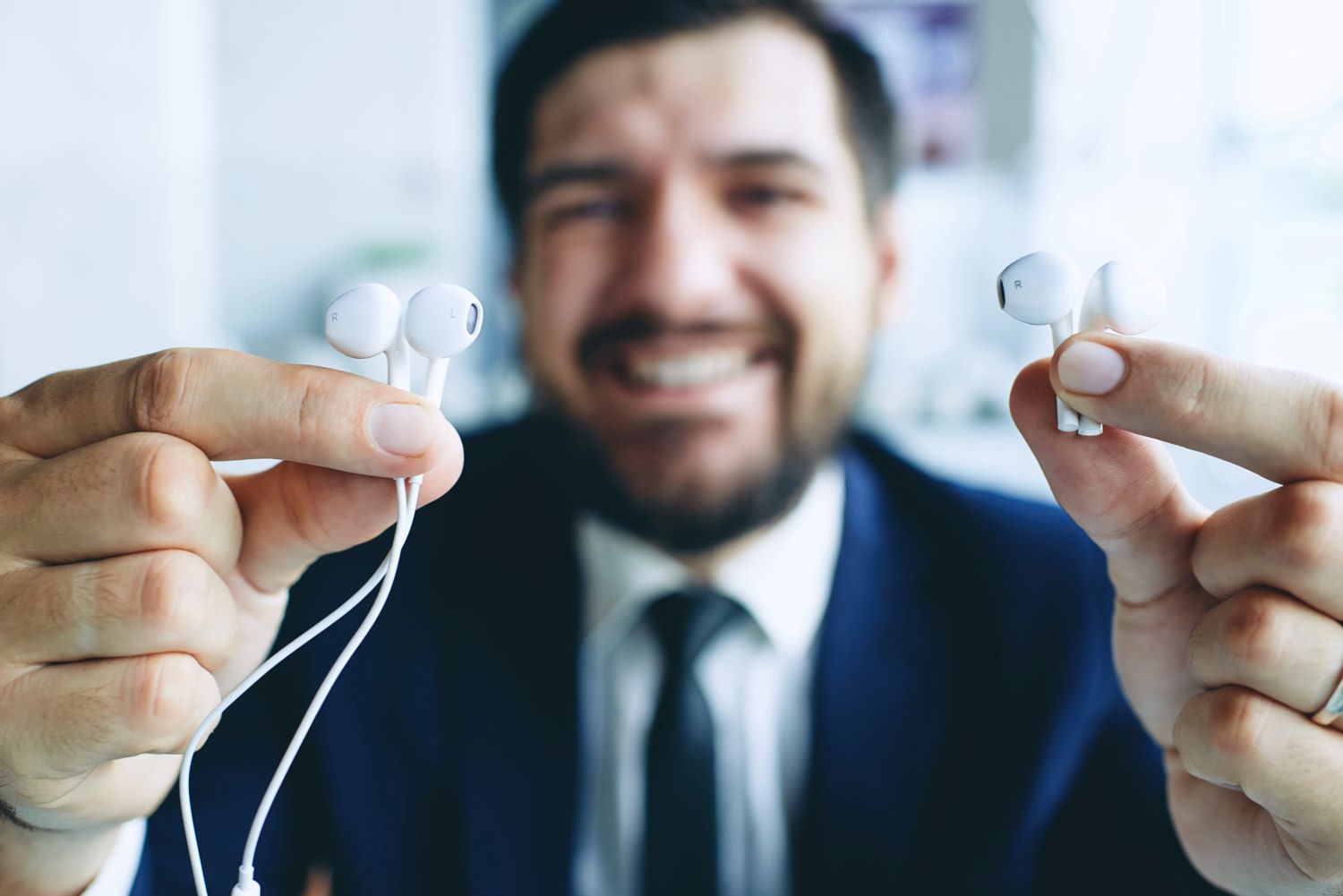 Un empresario con auriculares con cable en una mano y auriculares sin cable en la otra
