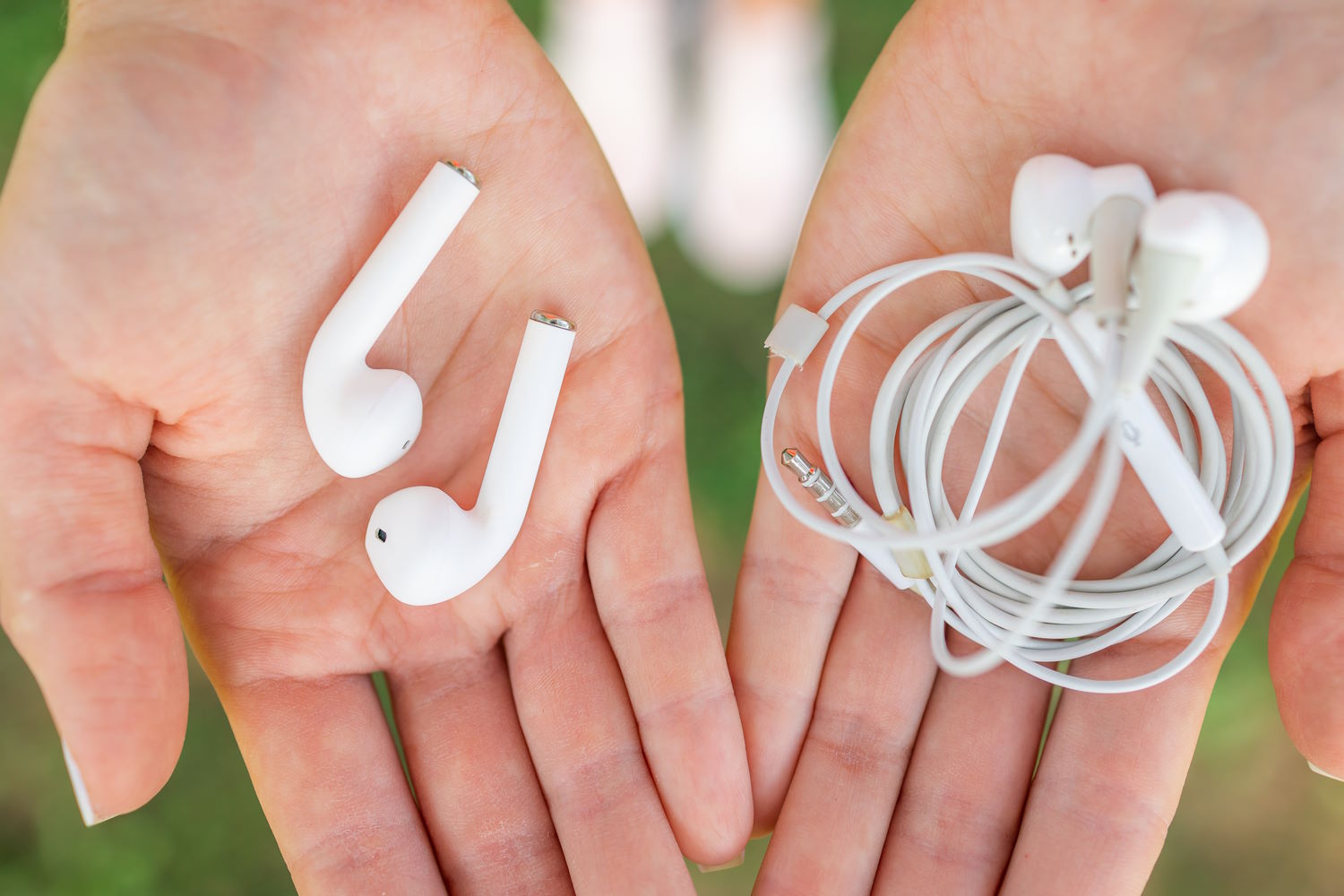 Una persona sostiene unos auriculares con cable en una mano y unos sin cable en la otra mano